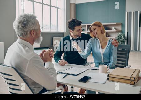 Glückliches junges Paar, das die Schlüssel einer neuen Wohnung erhält, während er im Büro des Immobilienmaklers sitzt Stockfoto