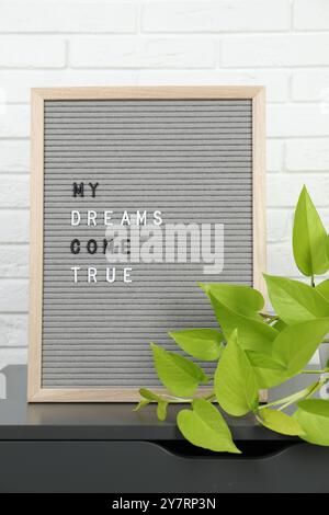 Brieftafel mit dem Spruch My Dreams Come True und Pflanzen Sie auf einem Beistelltisch in der Nähe der weißen Ziegelwand Stockfoto