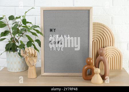 Brieftafel mit dem Satz My Dreams Come True, Pflanzen- und Dekorationselemente auf Holztisch in der Nähe der weißen Ziegelwand Stockfoto