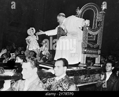 DER PAPST SEGNET KINDER viele Kinder waren in der großen Menge von Pilgern, die der Papst diese Woche in der Audienz des Petersdoms empfangen hat, bevor er Rom zu seinem Sommerpalast nach Castelgandolfo verlässt. Das Foto zeigt Papst Pius XII. Lehnt sich von seinem Stuhl, um das Gesicht eines kleinen Kindes zu berühren, das ihn schüchtern ansieht, als es aus der Menge gehoben wird. 15. Juli 1953 Stockfoto