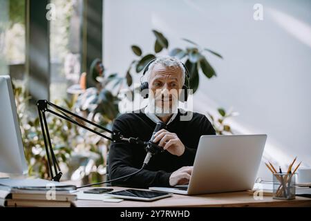 Selbstbewusster, ausgereifter Moderator, der Audiogeräte verwendet, während er Podcasts im Studio aufnimmt Stockfoto