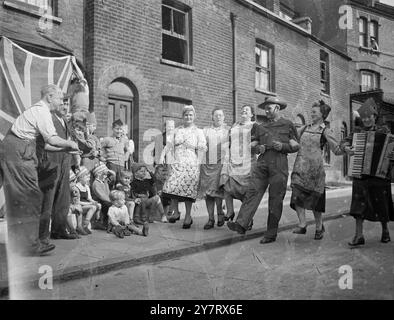 Die Leute von Kimpton Road, Camberwell, S.E. London, ergreifen den Arm eines vorbeiziehenden australischen Soldaten, der zur Krönung hier ist, und Proben einen guten alten "London Jig" in der Melodie eines Akkordeons, während sie sich auf ihre Krönungsfeier heute Nachmittag vorbereiten. Die Kinder auf der linken Seite finden es sehr lustig. Mai 1953 Stockfoto