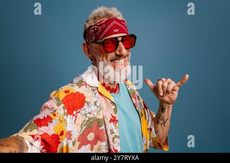 Hipster-Senior-Mann in stilvollem funky-Shirt und trendiger Brille, die Selfie und Gesten auf blauem Hintergrund macht Stockfoto