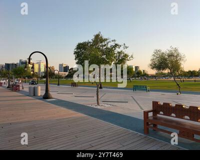 Holzbank und Wanderweg unter einem Baum in einem öffentlichen Park, Doha Stockfoto