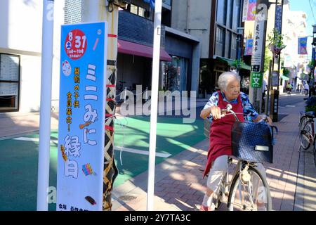 Eine ältere Frau, die auf der Sugamo Jizou-dori Shopping Street Fahrrad fährt. Toshima City, Tokio, Japan Stockfoto