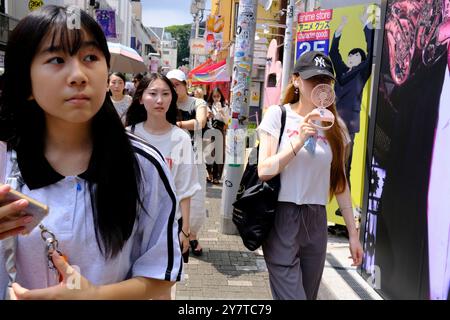 Eine junge Frau, die einen tragbaren Handventilator benutzt, um sich an einem heißen Sommertag in der Takeshita Straße abzukühlen. Harajuku, Shibuya Bezirk. Tokio, Japan Stockfoto