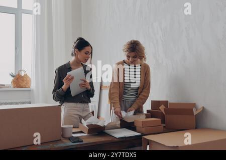 Zwei konzentrierte junge Frauen, die Pakete für die Lieferung am Arbeitsplatz vorbereiten Stockfoto