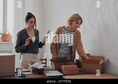 Zwei schöne junge Frauen, die Pakete für die Lieferung am Arbeitsplatz vorbereiten Stockfoto