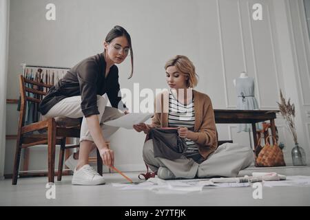 Zwei selbstbewusste Modedesignerinnen arbeiten zusammen in der Werkstatt Stockfoto