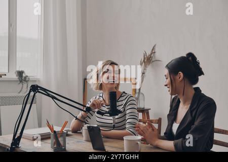 Zwei schöne junge Frauen sprechen und lächeln, während sie gemeinsam im Studio Podcasts aufnehmen Stockfoto