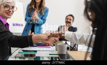 Meeting im Büro mit vielseitigem Team und Handschlag im Fokus. Generationenübergreifende und multiethnische Gruppen, die Vielfalt, Zusammenarbeit und Erfolg am Arbeitsplatz demonstrieren Stockfoto