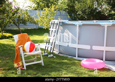 Oberirdischer Swimmingpool, Klappstuhl, Handtuch, aufblasbarer Ring und Ball im Hinterhof Stockfoto