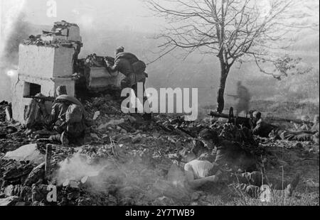 RACHE UND BARMHERZIGKEIT AUF DEM RUSSISCHEN SCHLACHTFELD während die Rote Armee über die Ukraine vordringt und die Nazi-Invasoren in Richtung der polnischen Grenze wirft, rücken Krankenschwestern der Roten Armee mit den vorderen Truppen vor und versorgen die Verwundeten dort, wo sie fallen. Foto zeigt: Eine rote Amy-Krankenschwester kniet neben einem verwundeten russischen Soldaten und pflegt seine Wunde, während die Schlacht um sie herum tobt. Rauch steigt aus den Ruinen eines Bauernhauses auf, während Maschinenschützen und Schützen einer Einheit der sowjetischen Garde die sich zurückziehenden Nazis angreifen. Von einem einzigen Baum im kriegszerrissenen Garten flattern die Blätter des Herbstes bis zum 13. Novemb Stockfoto