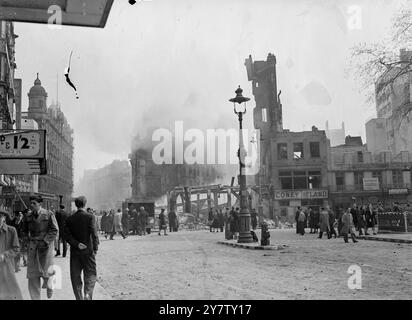 ARBEITER GEHEN AN BESCHÄDIGTEN GEBÄUDEN VORBEI NACH DEM SCHLIMMSTEN NAZI-ANGRIFF SEIT SEPTEMBER LETZTEN JAHRES Foto zeigt: Vor der abgerissenen Ecke eines Platzes GEHEN Arbeiter nach dem schlimmsten Sturz auf die Londoner Gegend seit dem großen Nazi-Angriff vom 17. April 1941 in ihre Büros Stockfoto