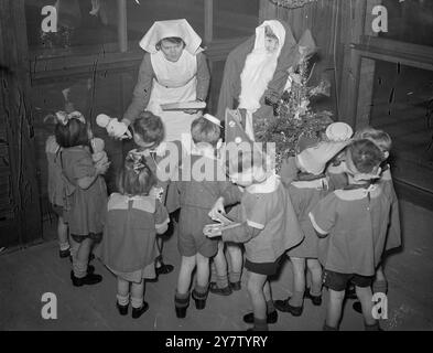 Eine WEIHNACHTSFEIER - TOTTENHAM DAY NURSERY, PARK LANE Children in a Day Nursery für Kinder unter fünf Jahren, deren Väter größtenteils in der Armee sind und ihre Mütter arbeiten, hatten trotzdem ein schönes Weihnachten. Foto zeigt: Eine Krankenschwester verteilt Geschenke an die eifrigen Kinder. Eines der Kinder trägt ein Weihnachtsmann-Outfit. 18. Dezember 1940 Stockfoto