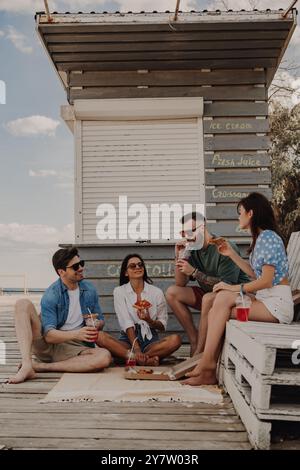 Eine Gruppe glücklicher Freunde genießt Pizza und Getränke, während sie sich in der Nähe des Strandcafés entspannen Stockfoto
