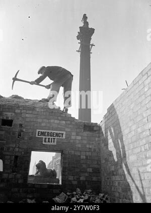 NELSON WENDET SICH DEN RÜCKEN ZU, während Großbritanniens Verteidigung abgerissen wird. Die Luftschutzbunker am Trafalgar Square werden endlich abgerissen. Auch in Friedenszeiten hatten sie ihre Verwendung, als Tribüne oder Pult für große öffentliche Versammlungen wie Sparkampagnen und ähnliches. Jetzt werden sie niedergerissen und Trafalgar Sauare wird wieder wie sein altes selbst aussehen, für die große Siegesparade am 8. Juni. - Foto zeigt: Ein Arbeiter schwingt seine Pistole auf dem alten Luftschutzbunker am Trafalgar Square, London, während der britische Löwe in der Öffnung eingerahmt ist. - 9. Mai 1946 Stockfoto