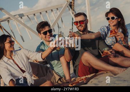 Gruppe von fröhlichen jungen Freunden, die mit Bier getoast und gemeinsam Pizza am Strand genießen Stockfoto