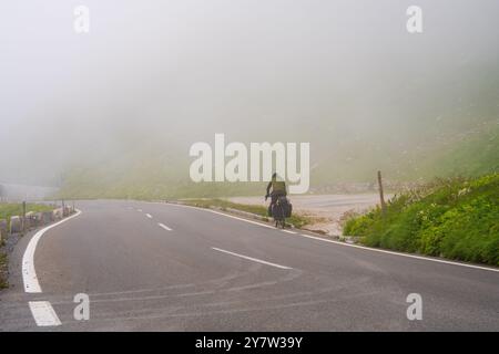 Sehr starker Nebel auf Bergstraßen. Radfahrer mit Gepäck auf der Großglockner Hochalpenstraße. Sehr schlechte Sicht durch Nebel. Serpentine, kurvenreiche Straße Stockfoto