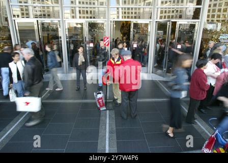 San Francisco, Kalifornien,... Mobs von Feiertagseinkäufern verlassen Macy's Kaufhaus am Union Square mit Taschen gefüllt mit Waren am Black Friday, dem 26. November 2004, dem offiziellen ersten Einkaufstag der Weihnachtszeit. Ein Arbeiter der Heilsarmee sammelt Spenden. Stockfoto