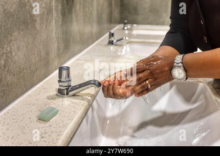 Person, die Hände in der Toilette wäscht, afroamerikanischer Mann Hände in Bewegung unter Wasser am Wasserhahn im öffentlichen Waschraum Stockfoto