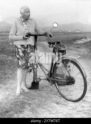 Eine ältere Frau radelt immer noch auf ihrem alten Fahrrad in ihrem ländlichen Ort Stockfoto