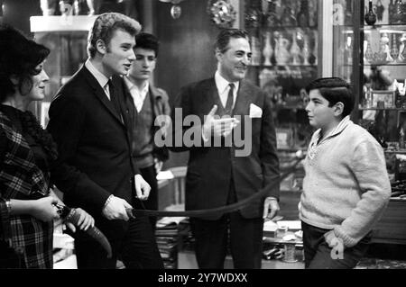 Eine riesige Menge von Fans und Nachrichtensprechern umzingelt den französischen Popsänger Johnny Hallyday (Mitte), als er am 24. November 1967 im Pariser Gerichtsgebäude ankam, um wegen Verkehrsdelikten zu erscheinen. Johnny Hallyday führt ein Schwert in einem Antiquitätenladen in Beirut, während er Souvenirs für sein mexikanisch-spanisches Haus in Paris kauft. Seine "Twist"-Show wurde in Beirut von den Behörden verboten. Januar 1963 Stockfoto