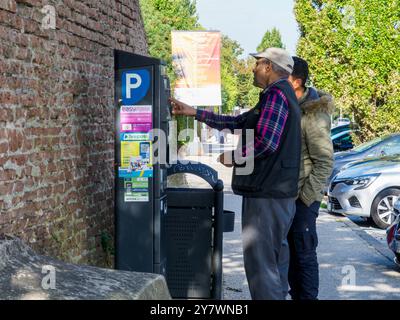 Mantua, Italien 30. September 2024 zwei Männer bezahlen ihren Parkplatz mit einer Parkuhr auf einer gepflasterten Straße neben einer Mauer Stockfoto