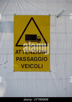 Mantua, Italien, 30. September 2024 Gelbes Warnschild mit schwarzem Rand, das einen vorbeifahrenden LKW zeigt, das auf einer weißen Kunststoffplatte auf einer Baustelle befestigt ist Stockfoto