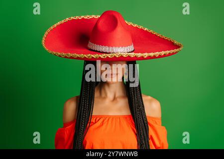 Wunderschöne junge mexikanische Frau in Sombrero, die vor grünem Hintergrund steht Stockfoto