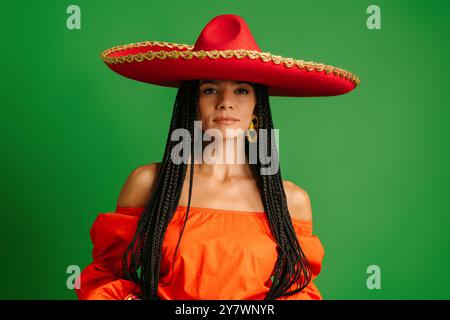 Wunderschöne junge mexikanische Frau in Sombrero, die vor grünem Hintergrund in die Kamera blickt Stockfoto