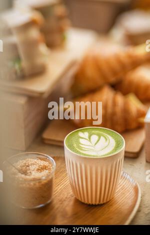 Tasse Matcha Latte umgeben von köstlichen Backwaren, in einem Café. Seitenansicht. Creme Latte Art. Schneidebrett aus Holz. Stockfoto