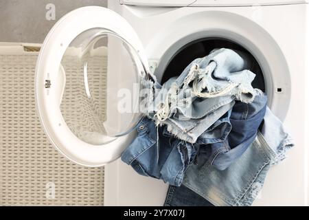 Waschmaschine mit schmutzigen Jeans und anderen Denim-Kleidern im Innenbereich Stockfoto