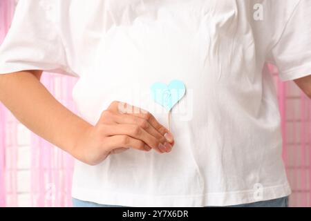 Schöne schwangere Frau mit Fragezeichen auf weißem Backsteinhintergrund, Nahaufnahme. Gender Reveal Party Konzept Stockfoto