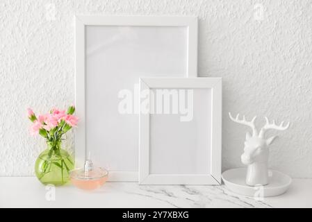 Schöne leere Bilderrahmen, Blumensträuße und Hirschfigur auf dem Tisch in der Nähe der weißen Wand Stockfoto