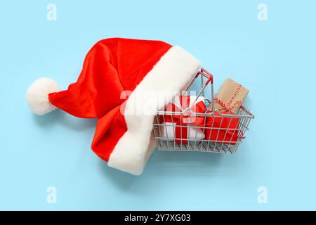 Mini-Einkaufskorb mit Weihnachtsgeschenken und Weihnachtsmann-Hut auf farbigem Hintergrund Stockfoto