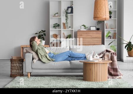 Junge Frau, die auf einem grauen Sofa im hellen Wohnzimmer liegt Stockfoto