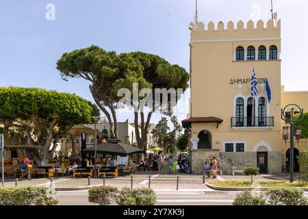 Rathaus, Restaurants und Altstadt mit Fußgängern an der Hafenpromenade von Kos-Stadt auf der Insel Kos in Griechenland Stockfoto