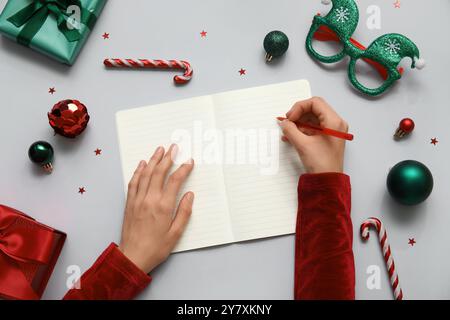 Frau schreibt Pläne für 2025 Jahre in Notizbuch und Weihnachtsdekor auf hellem Hintergrund Stockfoto