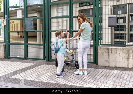 Junge High-Five und Abschied von seiner Mutter und dem kleinen kleinen Bruder am Schuleingang Stockfoto