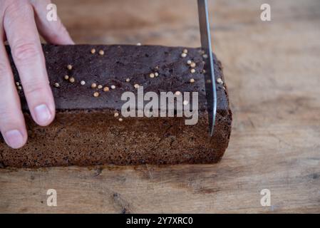 Roggenbrot in Scheiben geschnitten Foto. Der Mann schneidet Vollkorn-Roggenbrot auf einem hölzernen Schneidebrett. Stockfoto