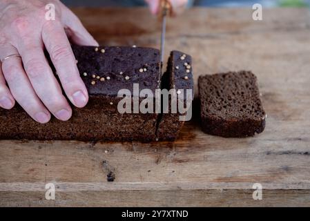 Roggenbrot in Scheiben geschnitten Foto. Der Mann schneidet Vollkorn-Roggenbrot auf einem hölzernen Schneidebrett. Stockfoto