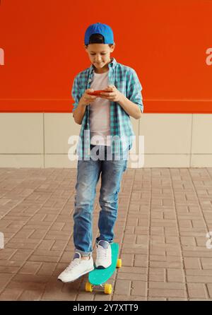 Glücklicher moderner Teenager mit Telefon, Skateboard, Kind mit Smartphone in der Stadt auf farbenfrohen roten Wand Hintergrund Stockfoto