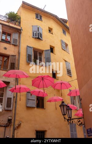 Rote Regenschirme hängen zwischen gelben Häusern, Parfümstadt Grasse, Provence-Alpes-Côte d'Azur, Frankreich Stockfoto