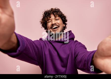 Tiefwinkelansicht eines glücklichen jungen Indianers, der Selfie vor rosa Hintergrund macht Stockfoto