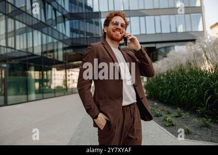 Ein selbstbewusster Geschäftsmann in einem braunen Anzug, der sich im Freien an Telefongesprächen beteiligt Stockfoto