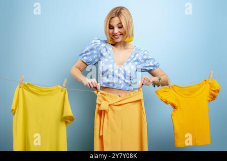 Eine attraktive junge Frau, die ihre bunten Kleider auf einem Wäscheleinen vor blauem Hintergrund hängt Stockfoto