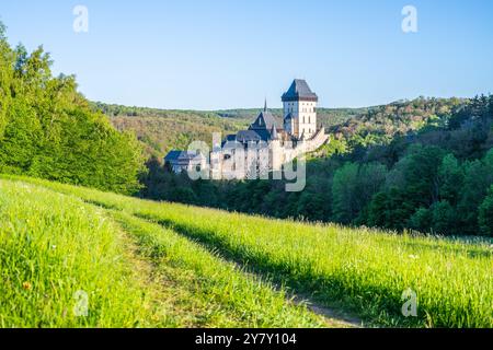 Ein ruhiger Blick auf das Schloss Karlstejn, das sich inmitten üppiger grüner Hügel in Tschechien befindet. Das Sonnenlicht strahlt ein warmes Licht aus und hebt die historische Architektur und die umliegende Natur hervor. Stockfoto