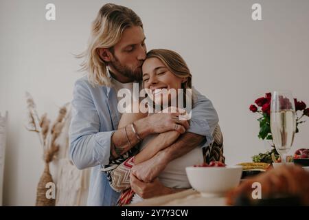 Junges, liebevolles Paar, das sich umschließt und küsst, während es ein romantisches Abendessen zu Hause zusammen genießt Stockfoto