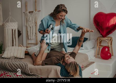 Verspielte junge Frau fotografiert ihren Freund mit Retro-Kamera, während sie sich zu Hause im Bett entspannt Stockfoto